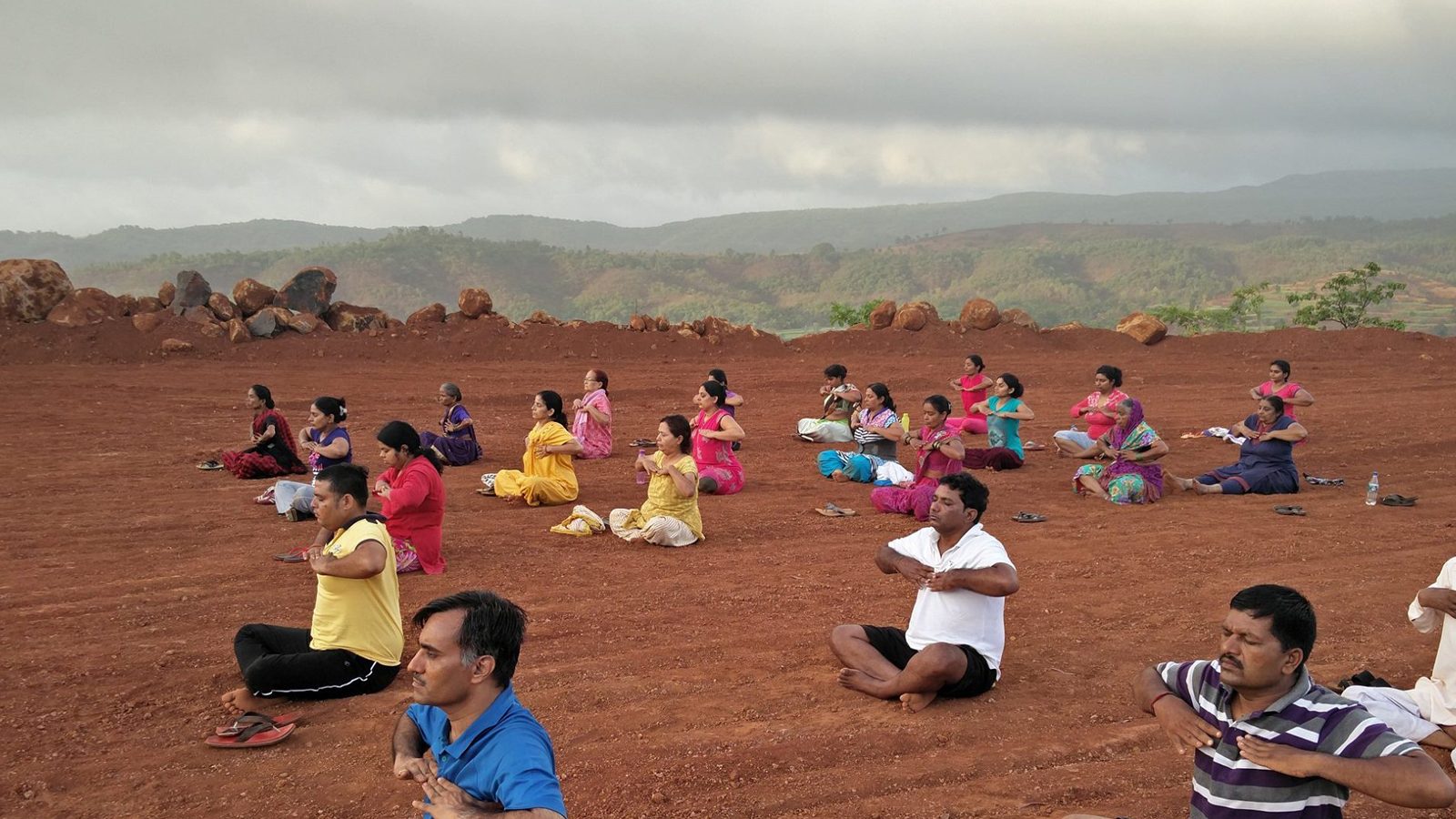 Group yoga session outdoors on red earth at Anandkunj