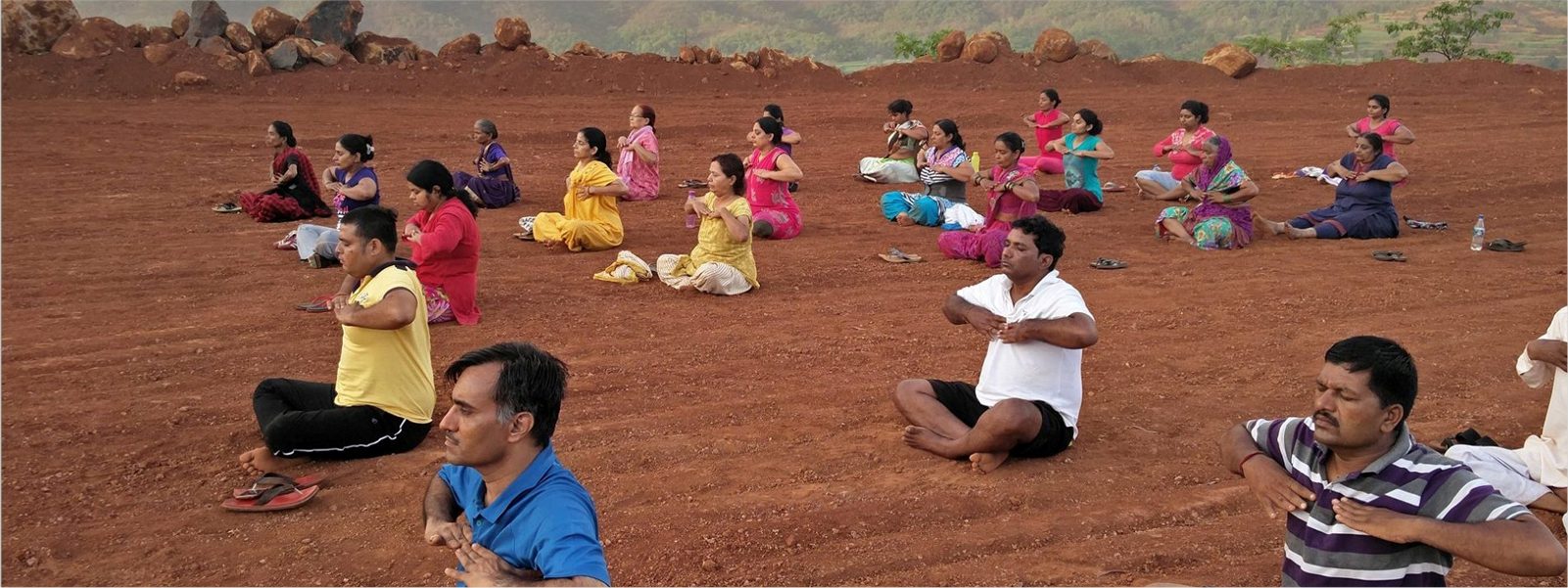 Group yoga session outdoors on red earth at Anandkunj